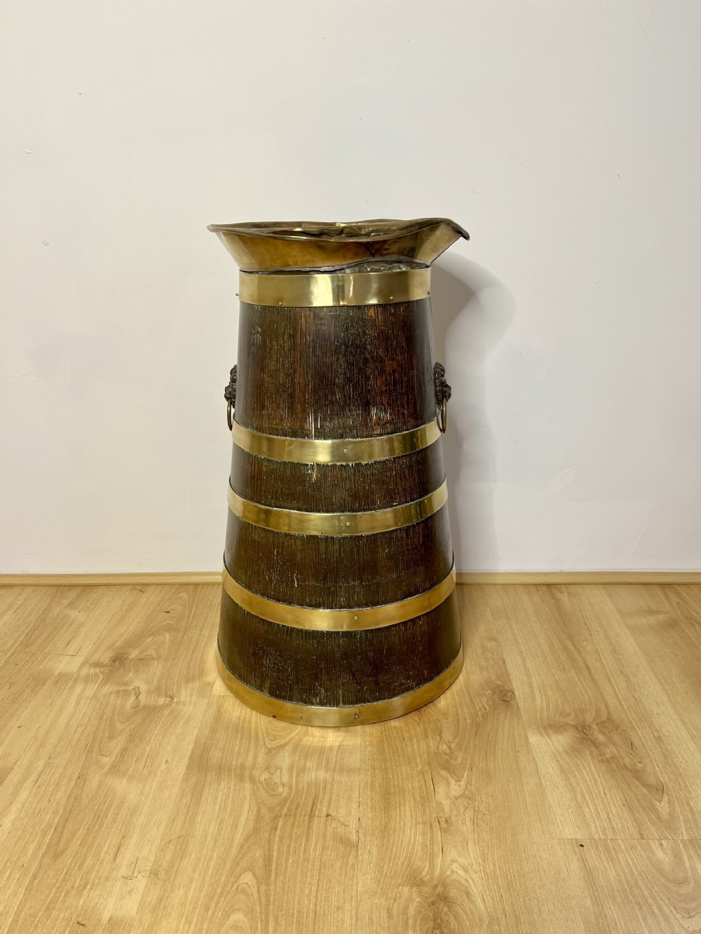 A dark oak Victorian stick stand featuring horizontal polished brass bands and lion mask ring handles.