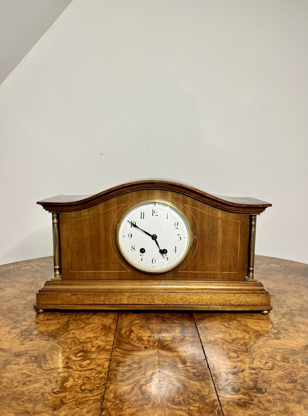 An Edwardian walnut mantel clock featuring an arched case, brass side columns, and a white dial with Arabic numerals.