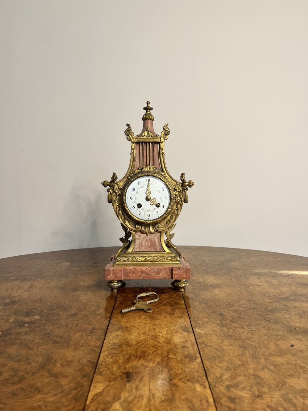 An antique French mantel clock crafted from pink marble and ornate gilt bronze mounts with a white enamel dial.