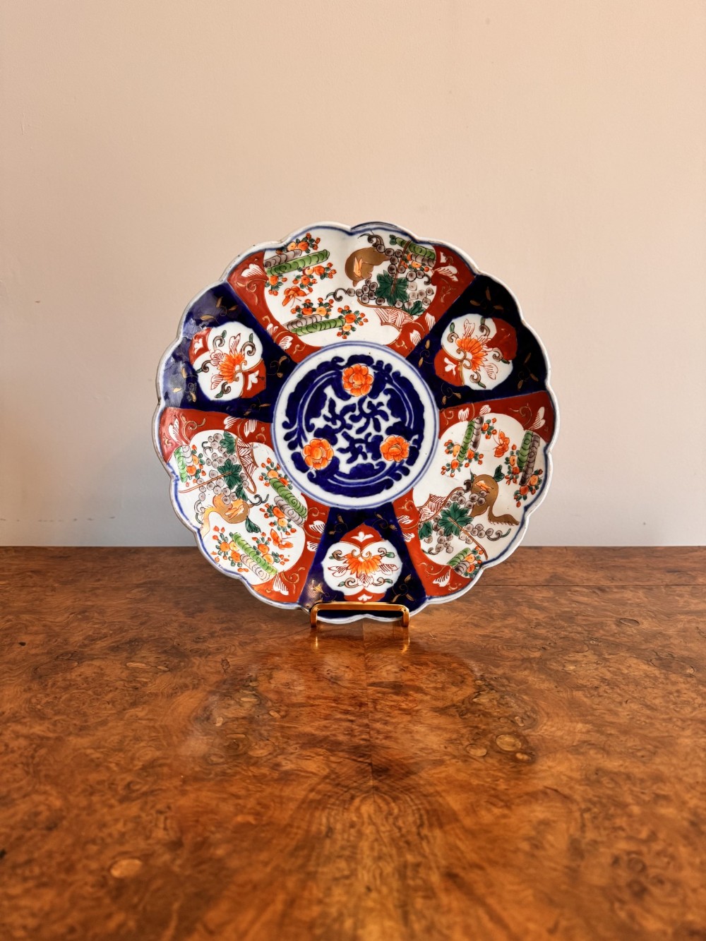 A circular Japanese Imari porcelain plate with a scalloped edge, decorated with cobalt blue, rust red, and green panelled floral patterns.