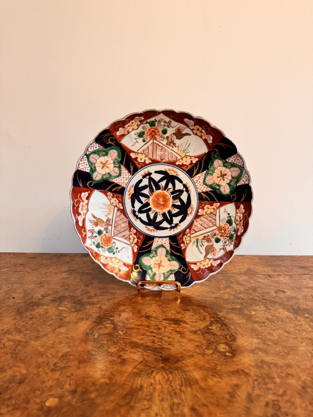 A circular antique Japanese Imari porcelain plate featuring a scalloped rim and detailed rust red, cobalt blue, green, and gilt floral panel decorations.