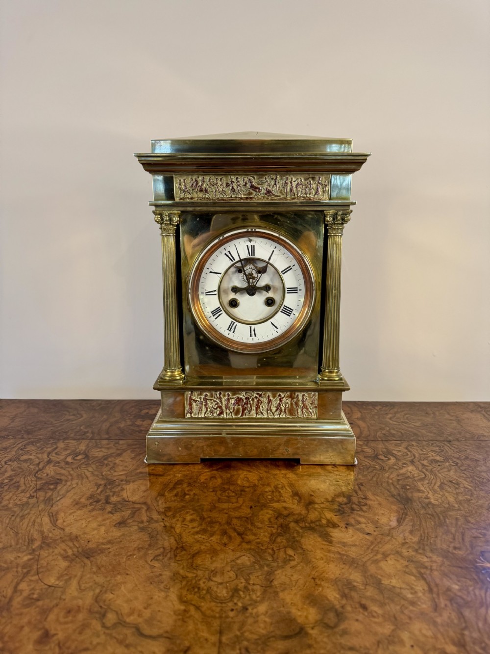 An antique brass mantel clock featuring fluted Corinthian columns, classical relief friezes, and a white enamel dial with Roman numerals.