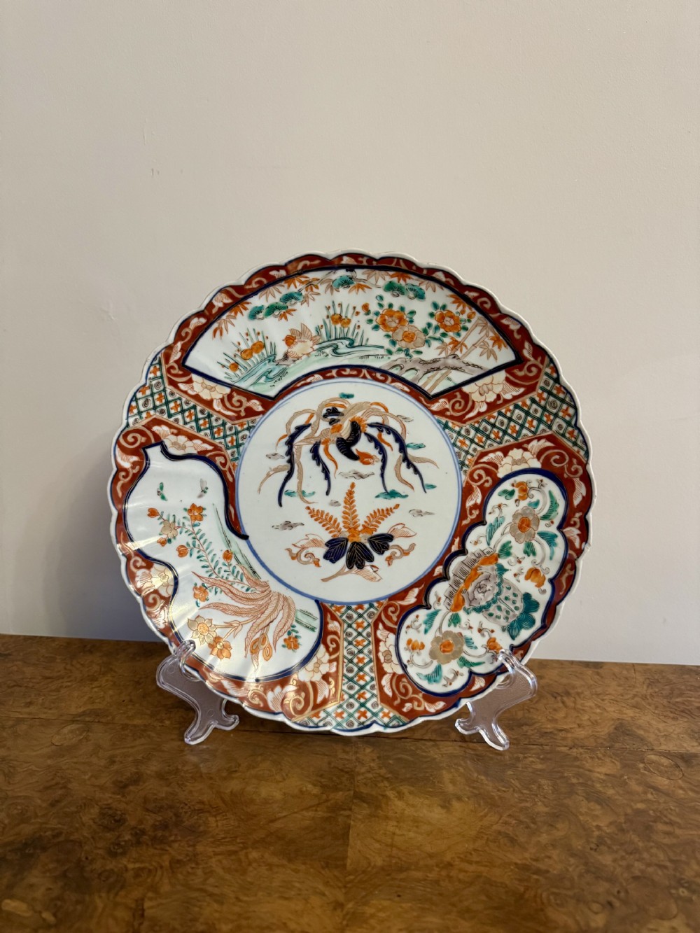 A circular antique Japanese Imari porcelain plate featuring a scalloped rim, central botanical motif, and radiating iron-red and cobalt blue patterned panels.