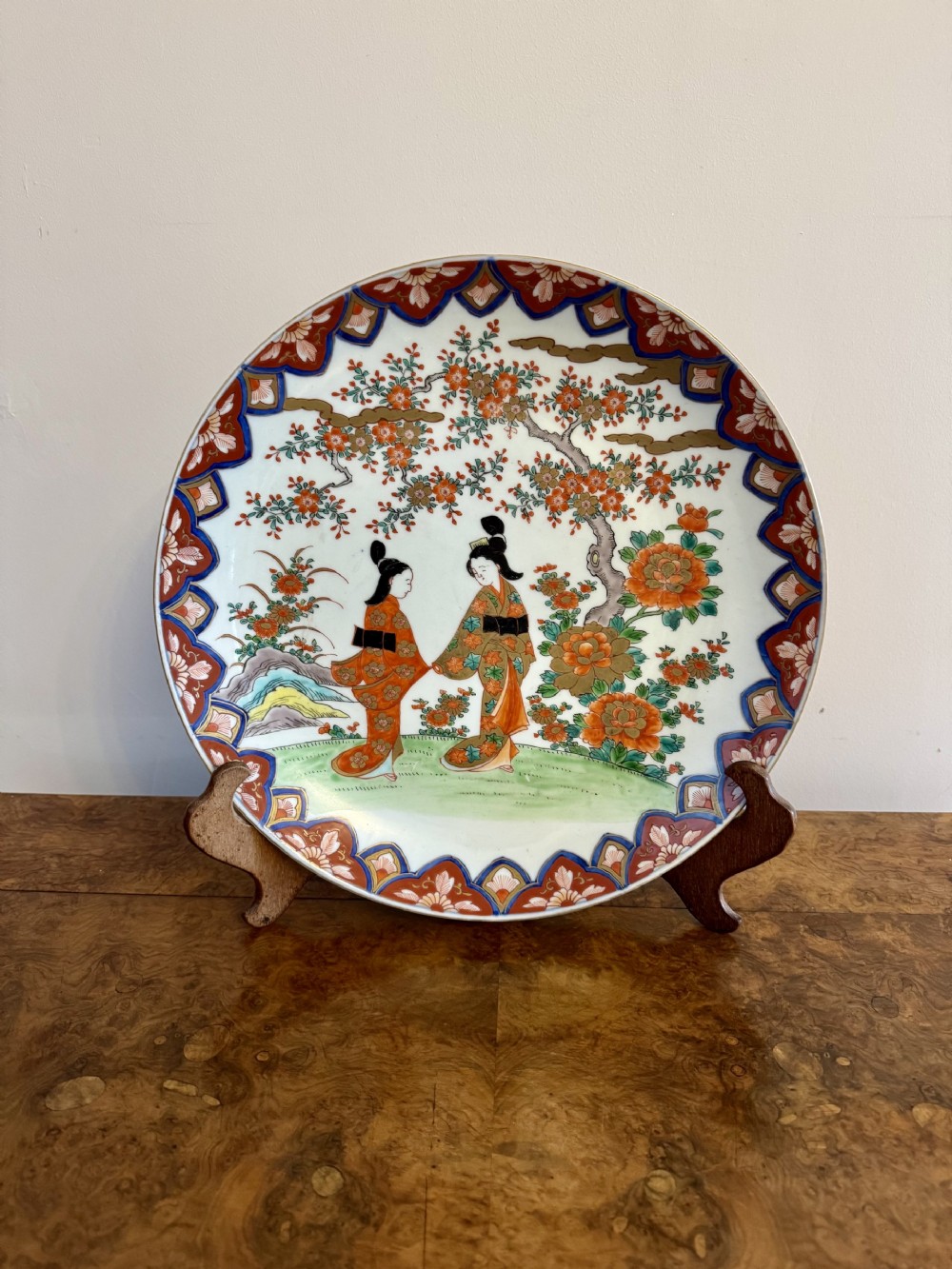 A circular Japanese Imari porcelain charger decorated with figures beneath a blossom tree surrounded by a patterned border.