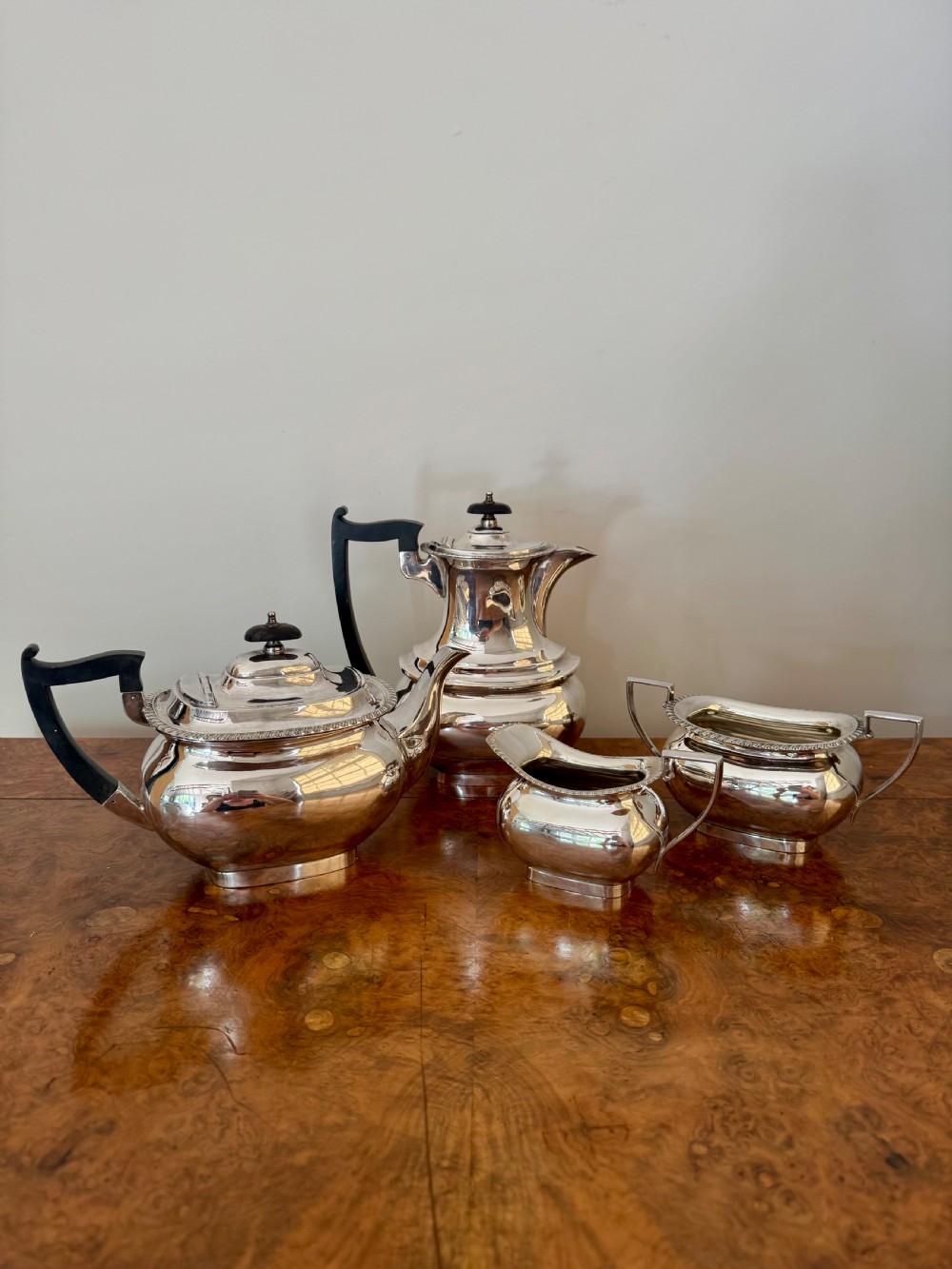 A four-piece Edwardian silver tea set comprising a teapot, coffee pot, cream jug, and sugar bowl with black wooden handles.