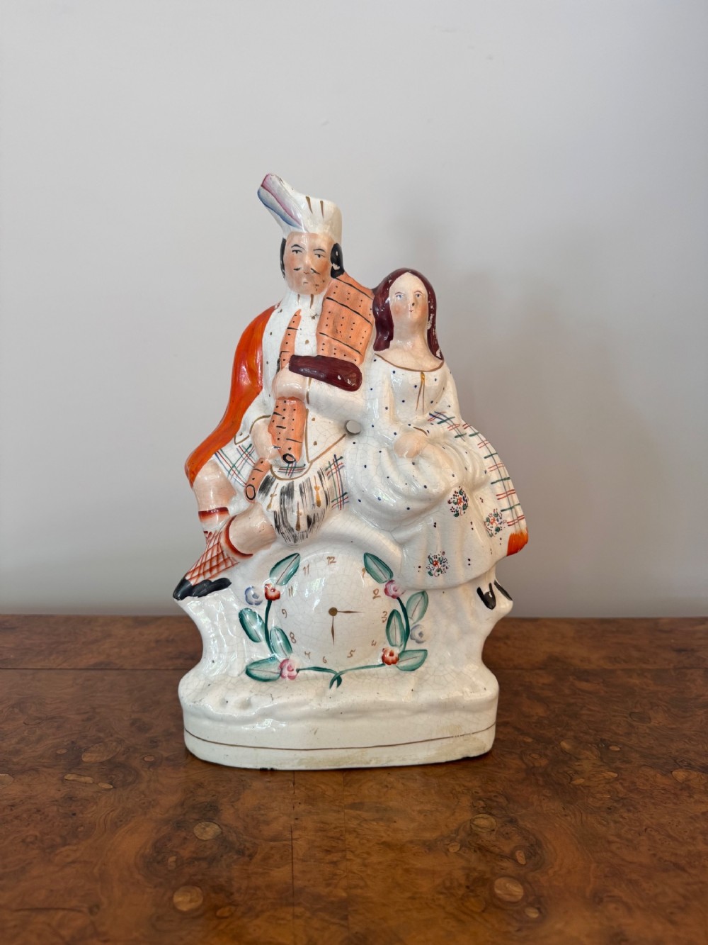 Victorian Staffordshire earthenware flatback figure featuring a Scottish man with bagpipes and a seated woman above a painted clock face.