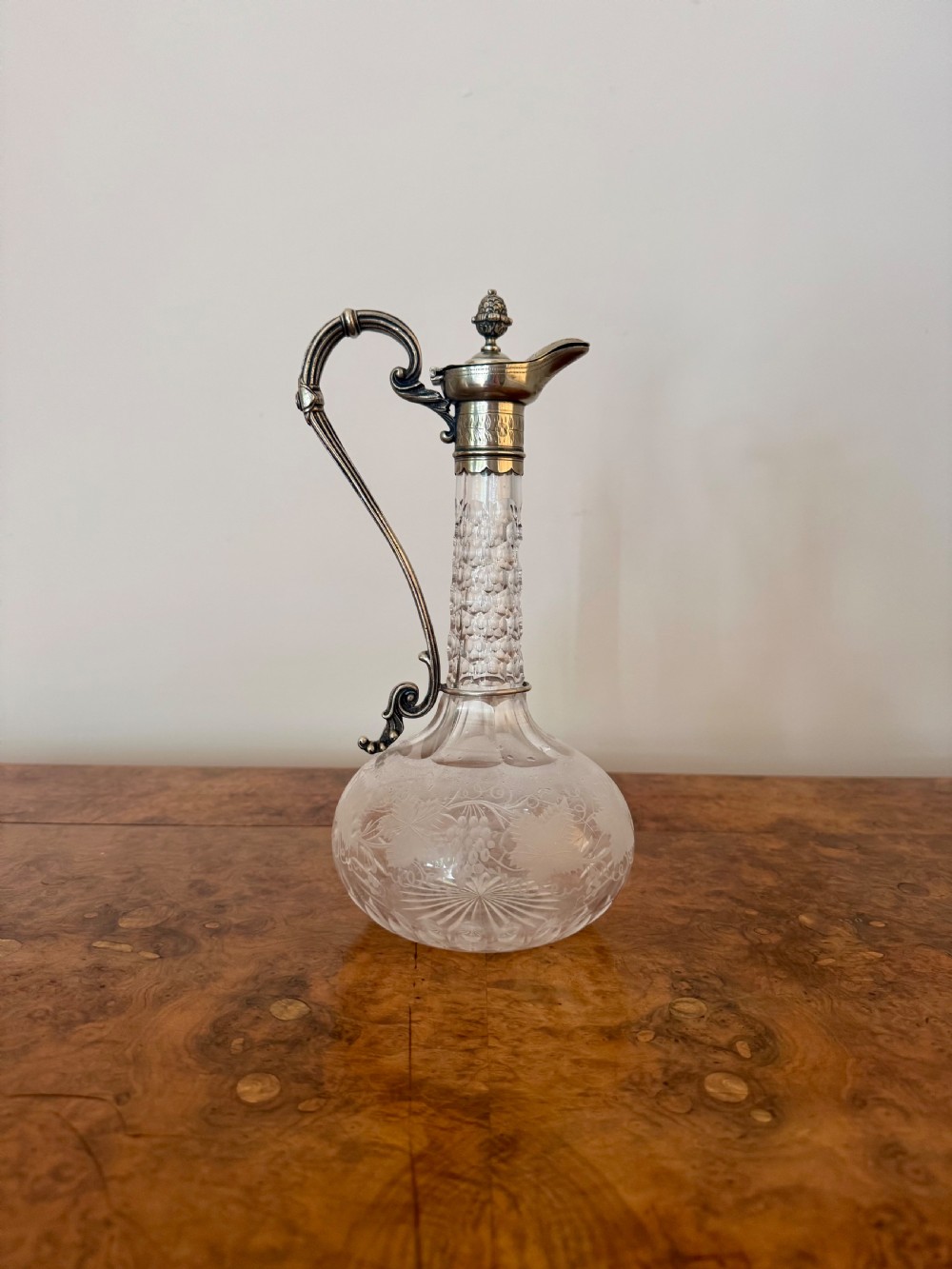 A Victorian clear etched glass claret jug featuring floral vine patterns, a textured glass neck, and a silver-plated collar with a scroll handle and finial lid.