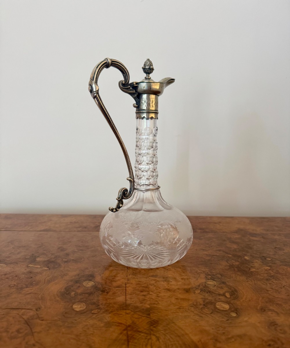 A Victorian clear etched glass claret jug featuring floral vine patterns, a textured glass neck, and a silver-plated collar with a scroll handle and finial lid. View II