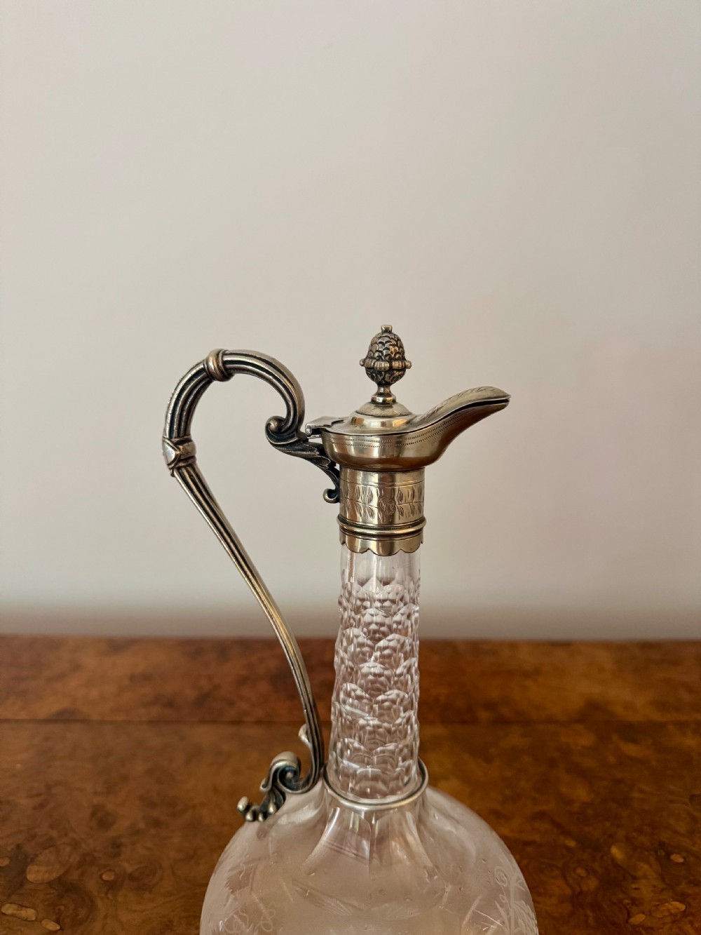 A Victorian clear etched glass claret jug featuring floral vine patterns, a textured glass neck, and a silver-plated collar with a scroll handle and finial lid. View VIII