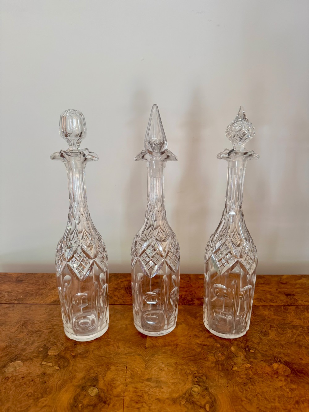 A trio of tall Edwardian clear cut glass decanters featuring geometric faceted stoppers and diamond cut pattern details. View II