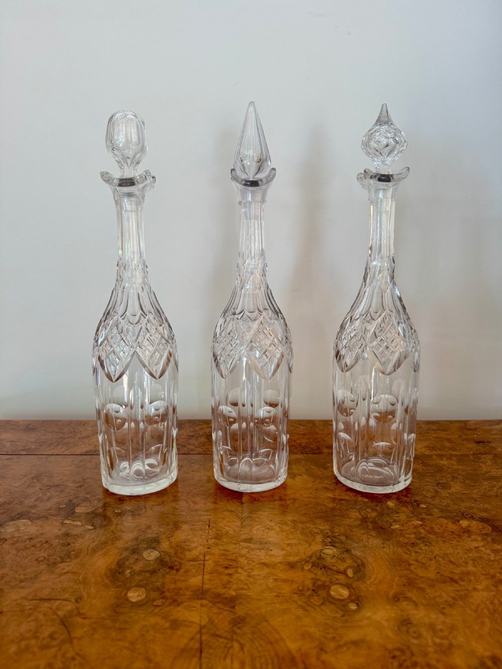 A trio of tall Edwardian clear cut glass decanters featuring geometric faceted stoppers and diamond cut pattern details.