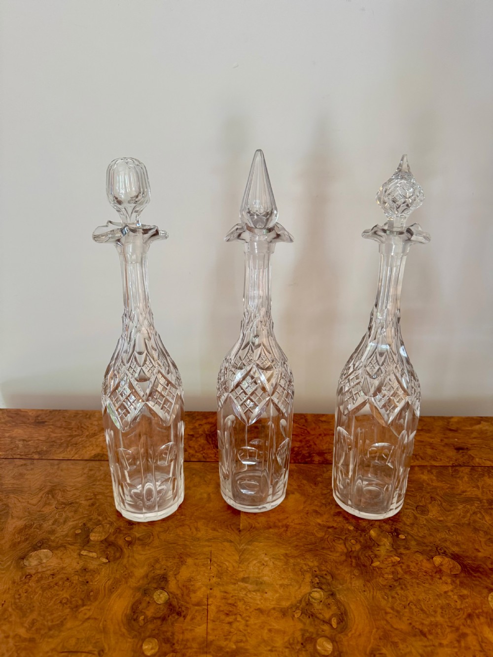 A trio of tall Edwardian clear cut glass decanters featuring geometric faceted stoppers and diamond cut pattern details. View III