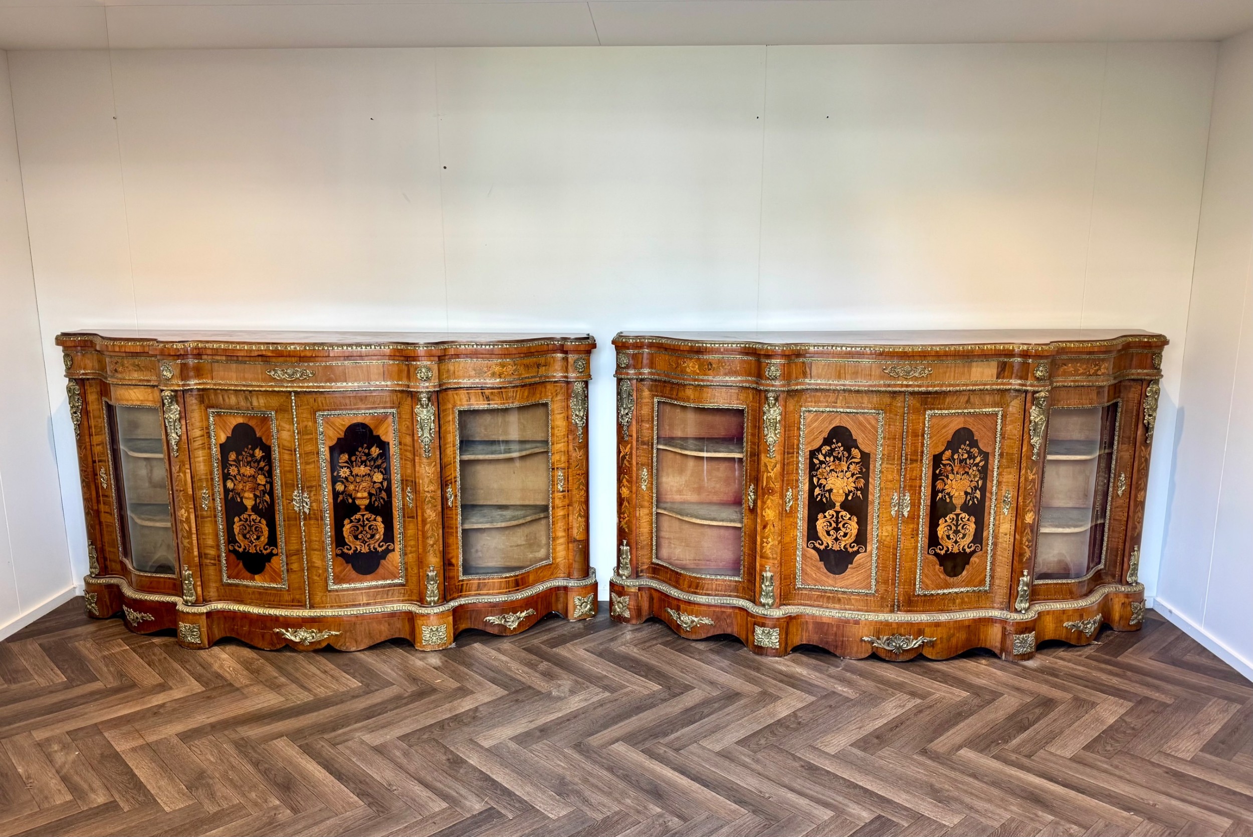 A pair of Victorian burr walnut credenzas featuring central ebonised panels with floral marquetry inlay, bow-front glass side doors, and gilt bronze mounts.