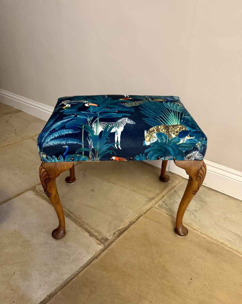 A Victorian carved walnut footstool featuring cabriole legs and patterned blue upholstery depicting wildlife.