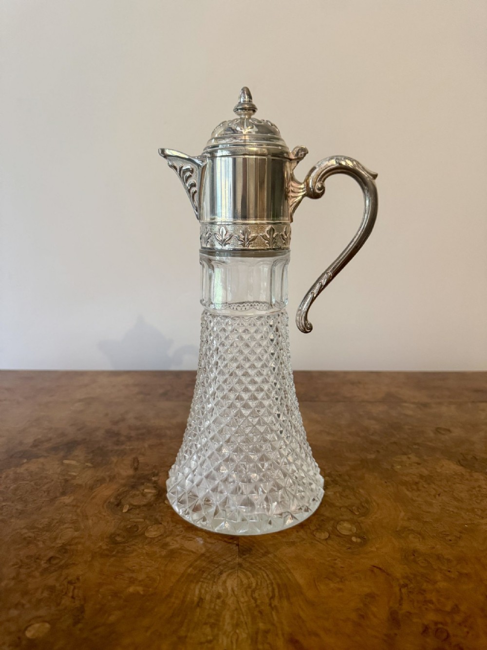 An Edwardian silver-plated and cut glass claret jug featuring a decorated hinged lid and scroll handle.