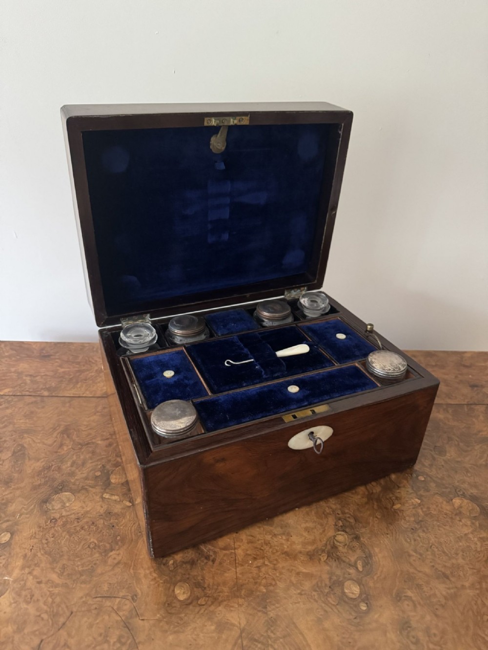 An open dark brown Victorian rosewood vanity box with a blue velvet-lined interior and fitted glass bottles.