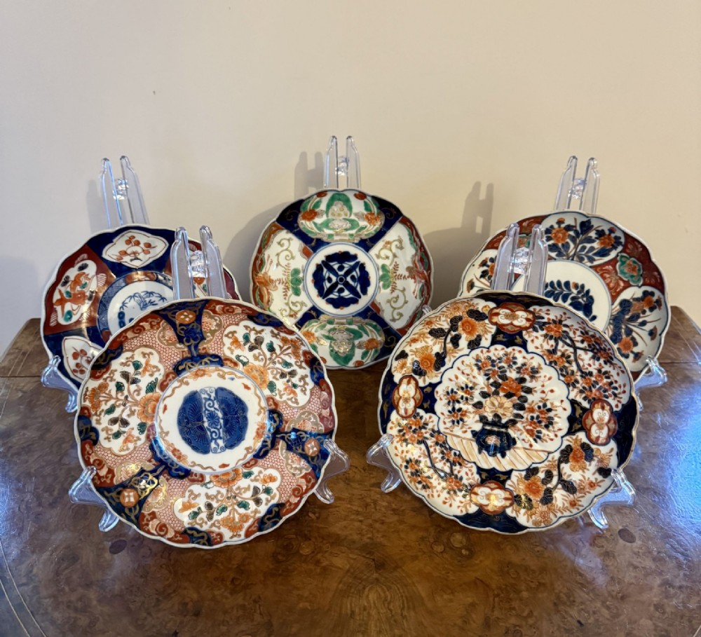 A collection of five Japanese Imari porcelain plates with scalloped edges and detailed floral patterns in cobalt blue, iron-red, and gold.