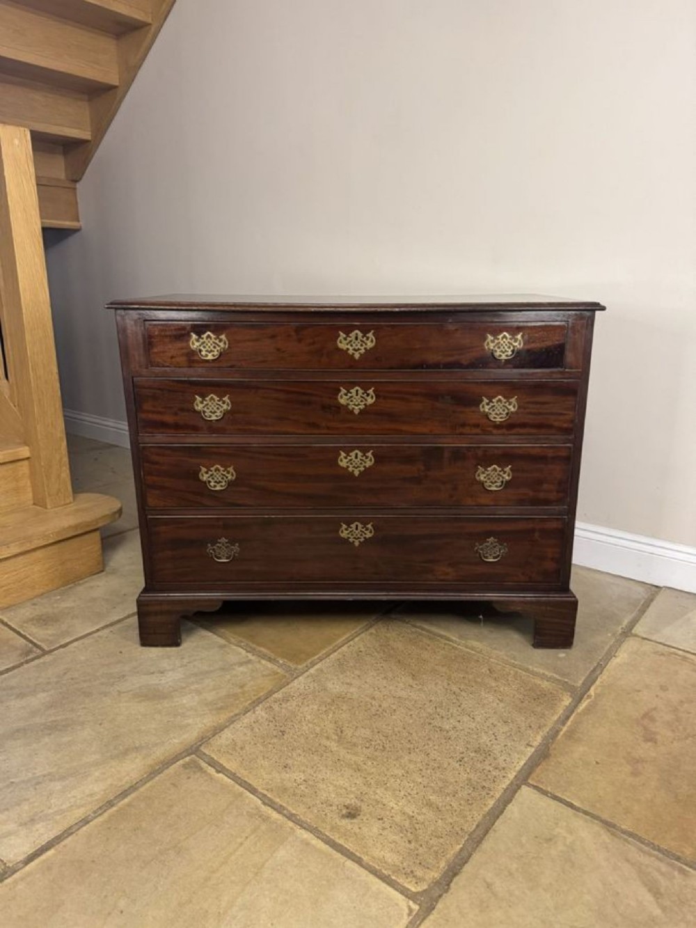 A George III mahogany chest of drawers with four graduated long drawers, ornate brass backplates, and sturdy bracket feet.