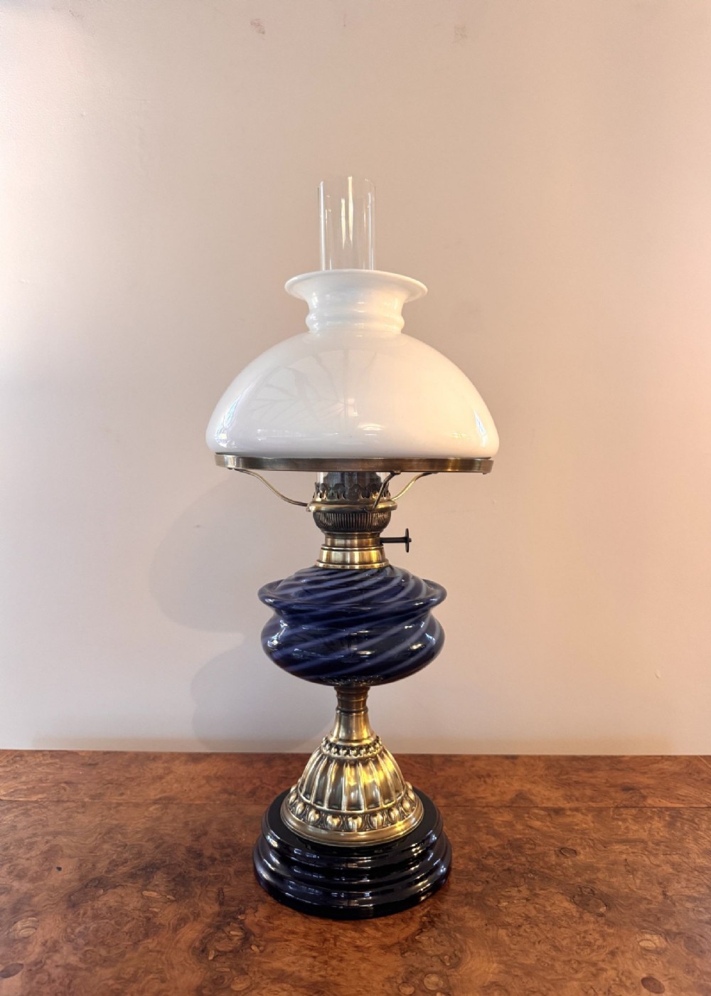 An Edwardian oil lamp featuring a black ceramic base, polished brass fittings, a cobalt blue swirl glass reservoir, a white dome glass shade, and a clear glass chimney.