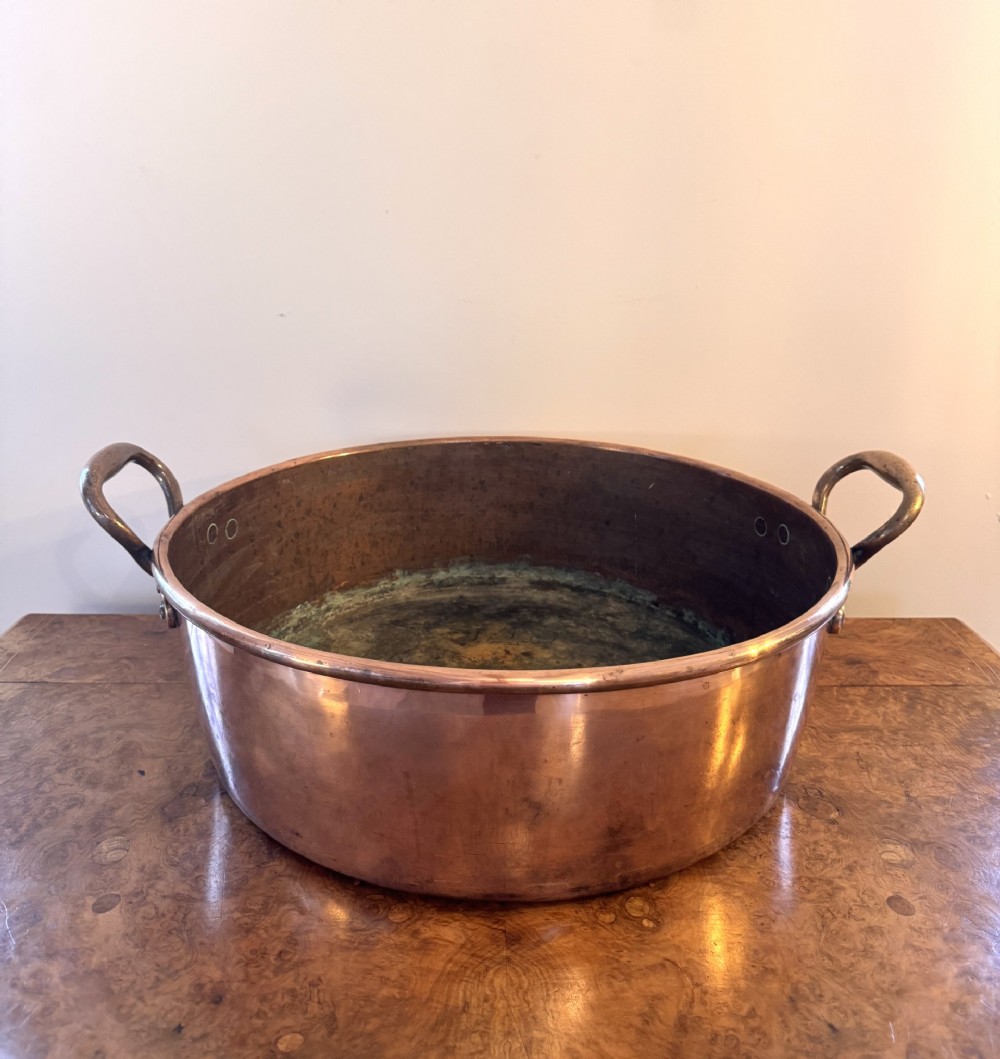 A large circular antique George III copper preserve pan featuring rolled rims and riveted side handles.