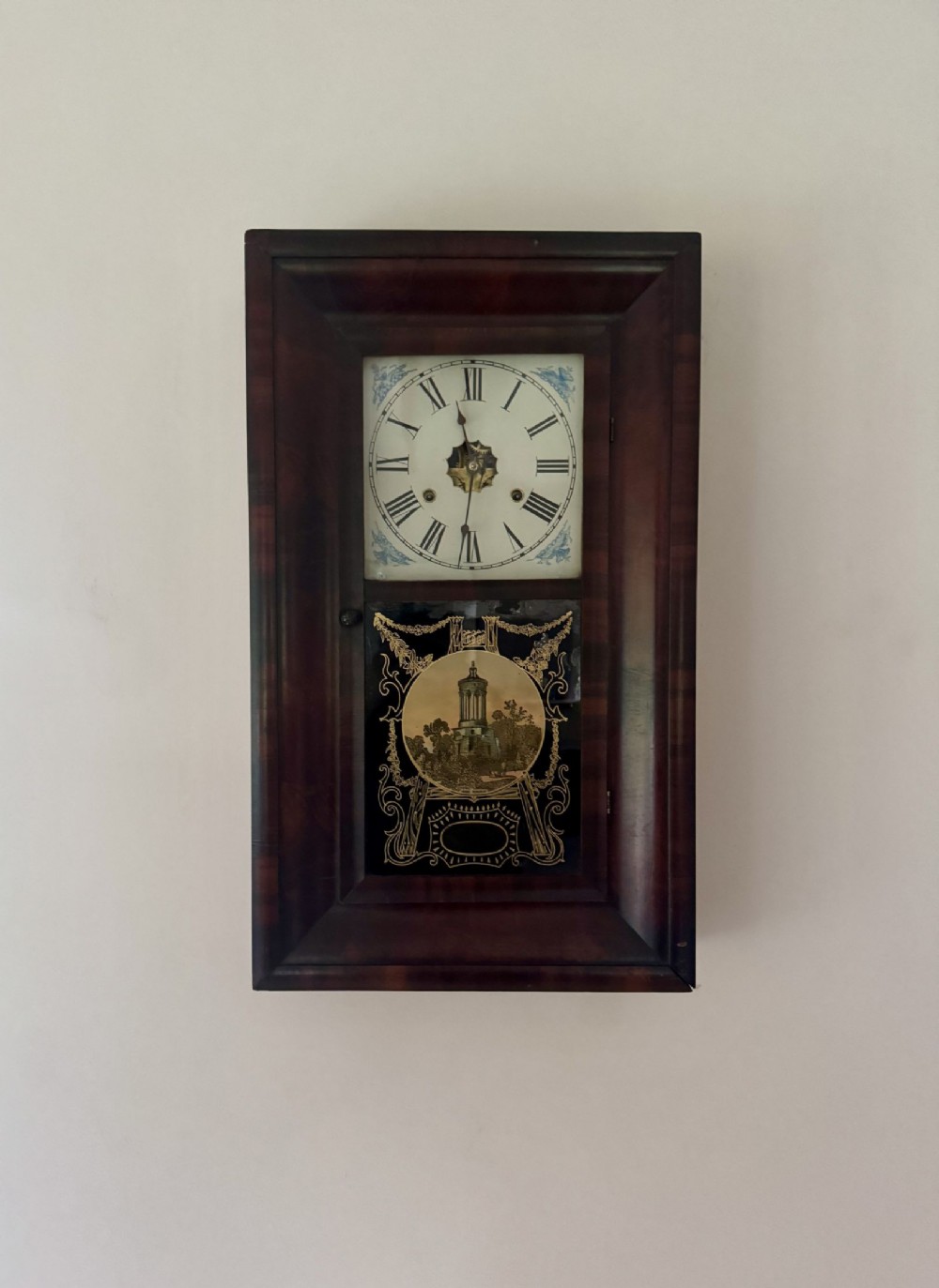 A 19th-century rectangular mahogany wall clock featuring a white painted dial with Roman numerals and a lower reverse-painted glass panel depicting a historic building.