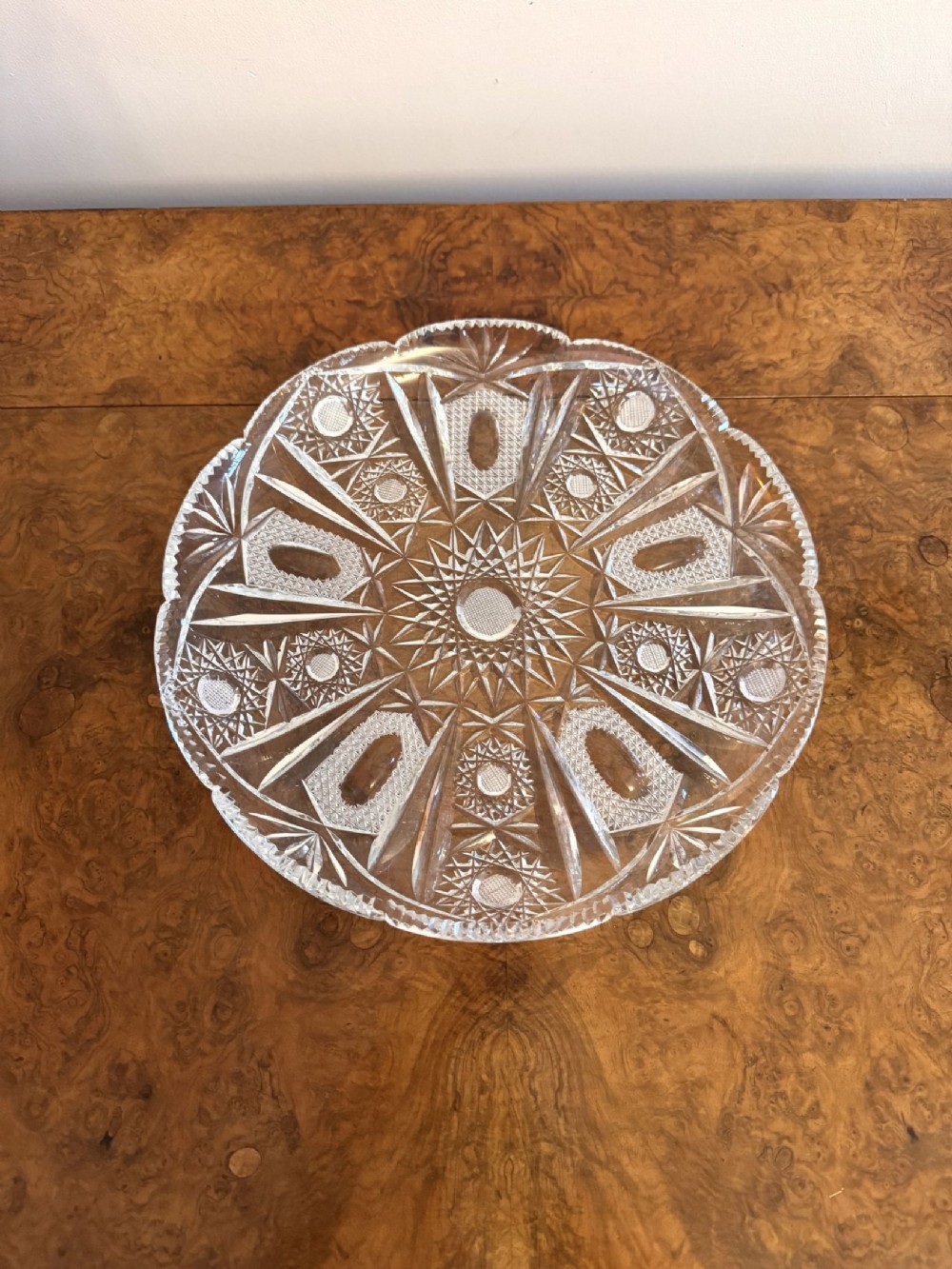 A circular clear Edwardian cut glass dish with a scalloped edge and geometric starburst wheel-cut pattern.