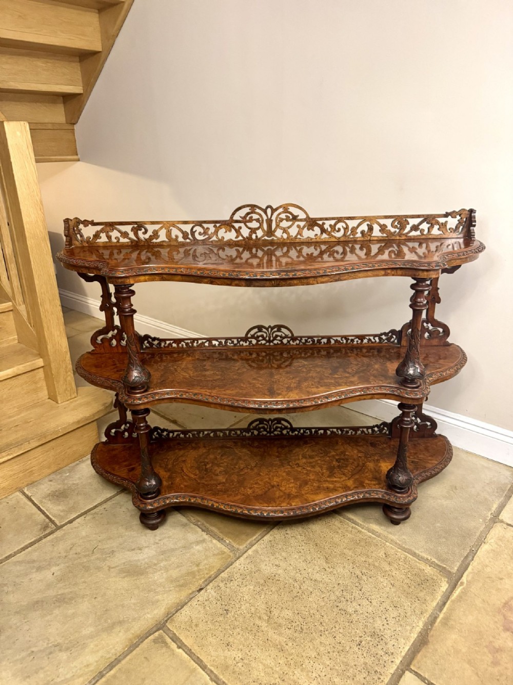 An antique Victorian three-tier whatnot made of figured walnut, featuring carved fretwork galleries, serpentine front shelves, and turned upright supports.