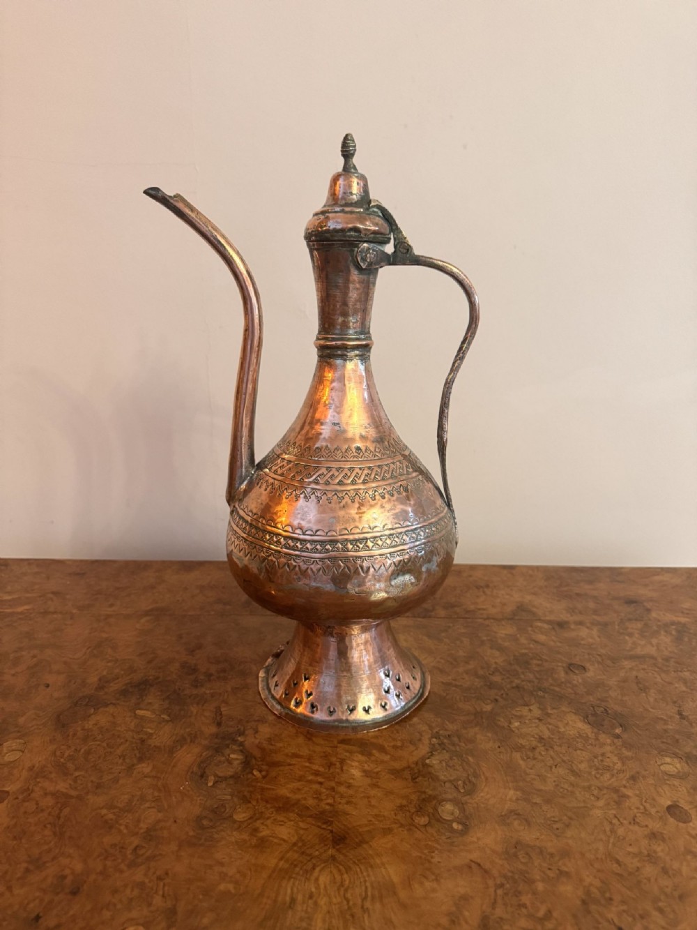A 19th-century Middle Eastern copper coffee pot featuring a long curved spout, intricate chased geometric patterns, and a pierced pedestal base.