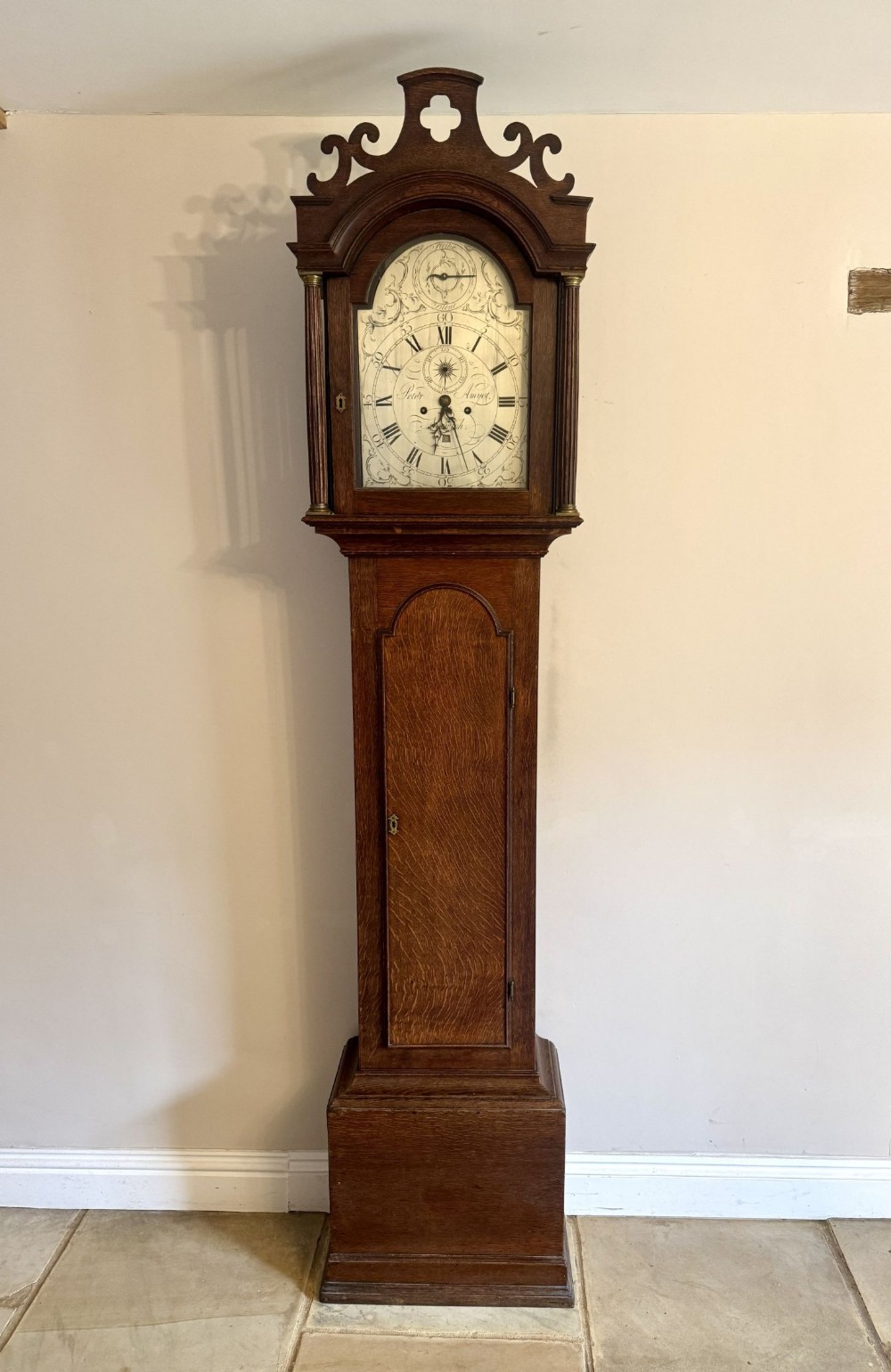 An antique George III oak longcase clock featuring an arched dial, decorative pediment, and a warm timber casing.