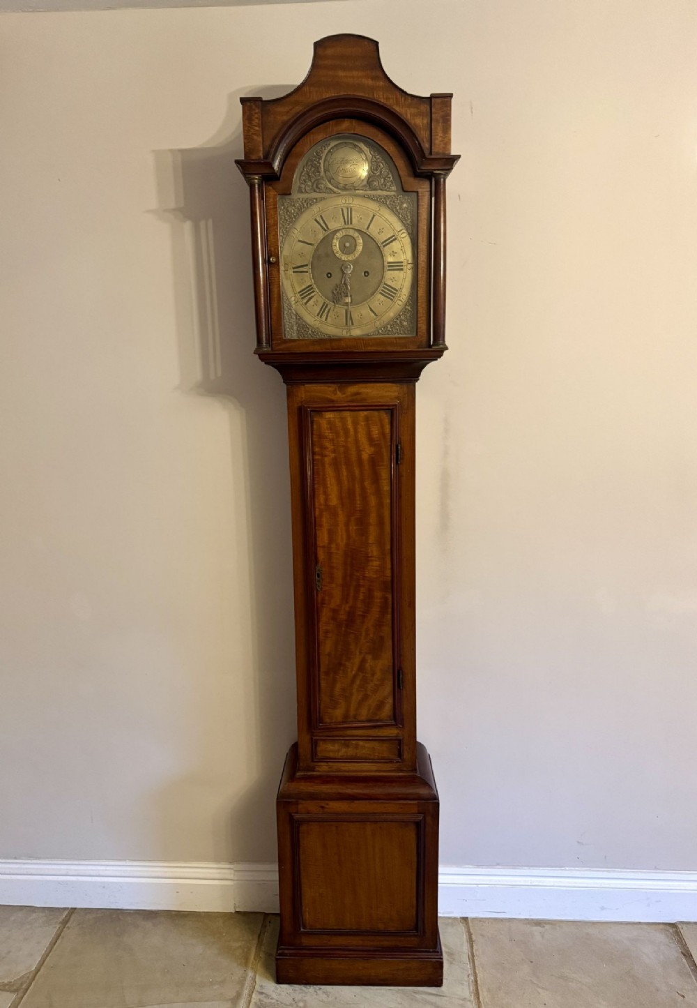 A George III flame mahogany longcase clock featuring an arched brass dial and turned columns on the hood.