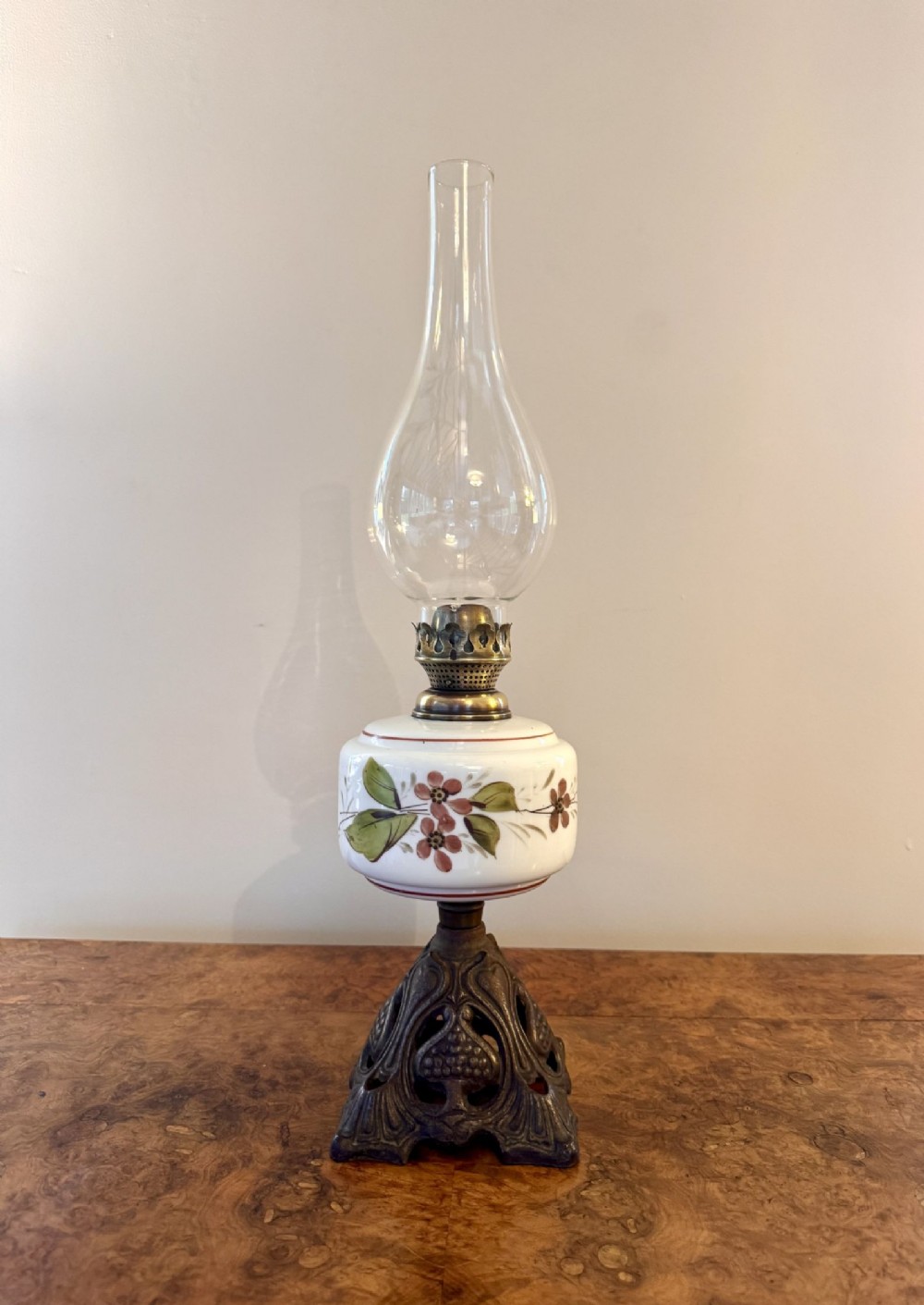 An antique Victorian oil lamp featuring a clear glass chimney, brass burner, white hand-painted glass reservoir with floral decoration, and dark ornate cast metal base.