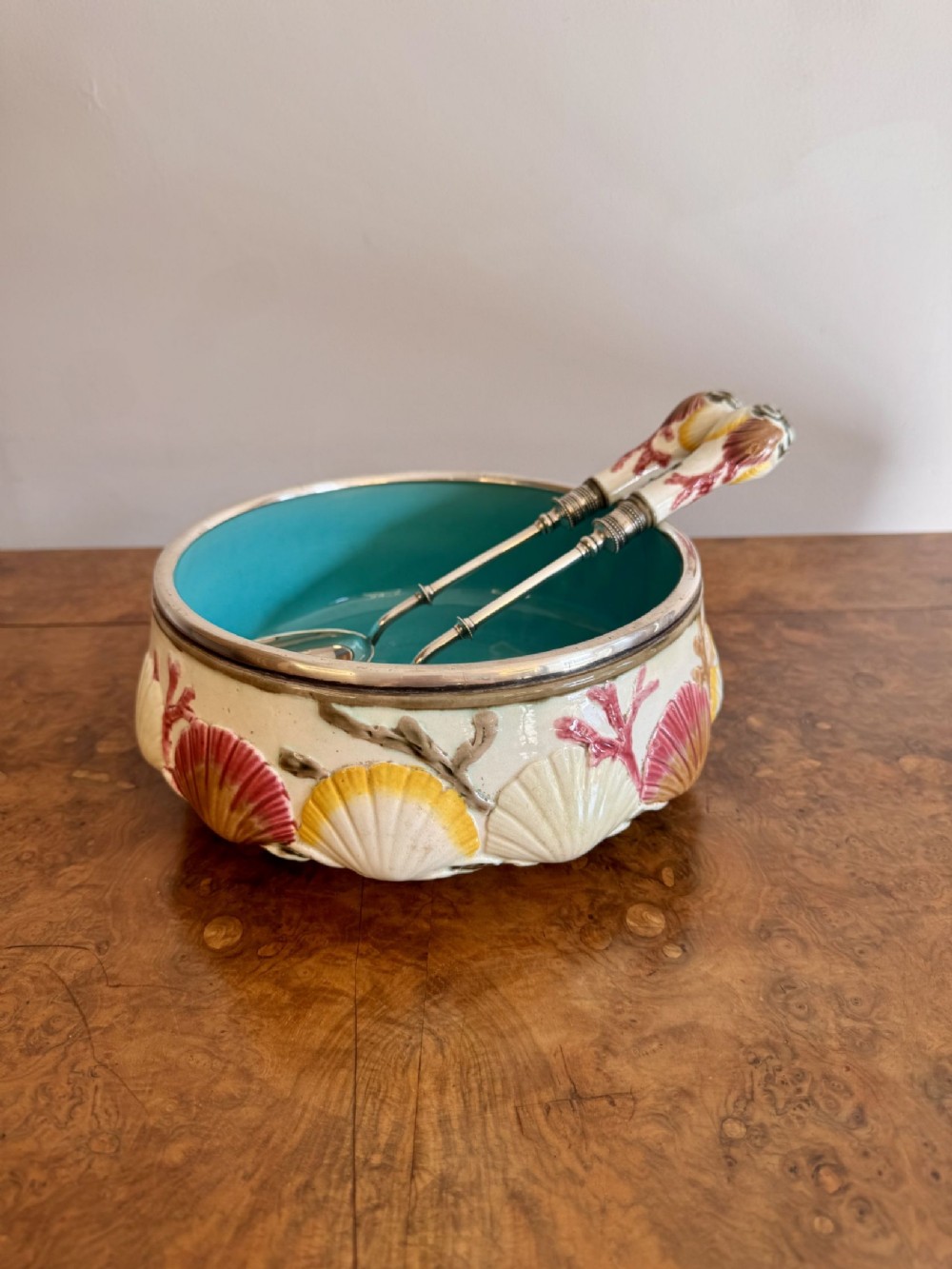 A nineteenth-century majolica salad bowl decorated with moulded relief seashells, a turquoise interior glaze, a silver-plated rim, and matching servers.
