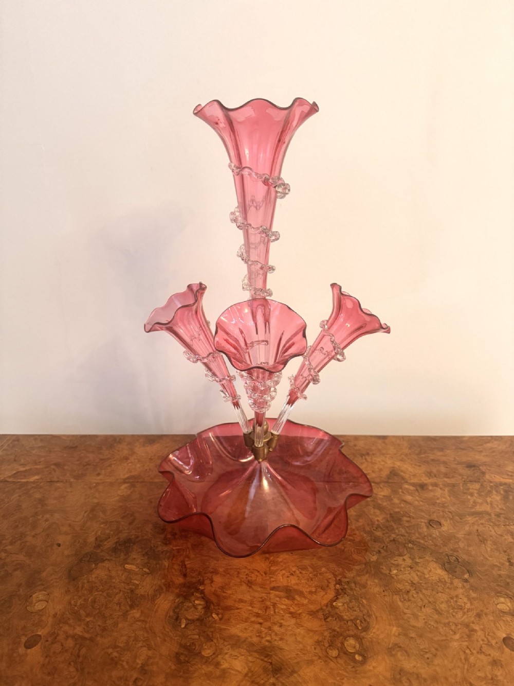 A Victorian cranberry glass epergne featuring a ruffled bowl base holding four trumpet-shaped flutes with applied clear glass trailing.