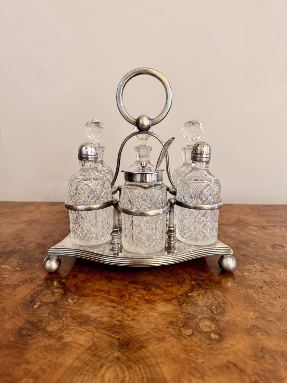 An Edwardian silver-plated cruet stand holding six cut-glass bottles with silver tops and a central looped carrying handle.