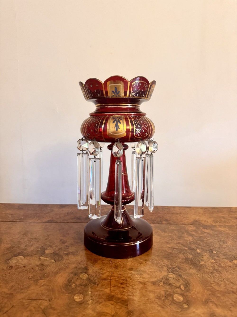 Victorian ruby red glass mantle lustre with hand-painted gilt decoration, white enamel accents, a scalloped rim, and suspended clear cut-crystal drop prisms.
