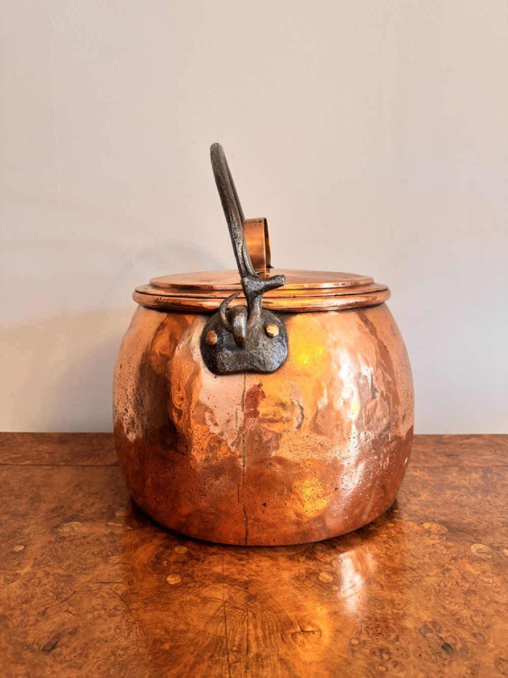 A large round hand-hammered copper pot with a fitted copper lid and a dark iron swing handle. View II