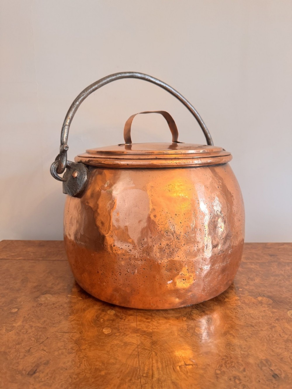 A large round hand-hammered copper pot with a fitted copper lid and a dark iron swing handle. View III