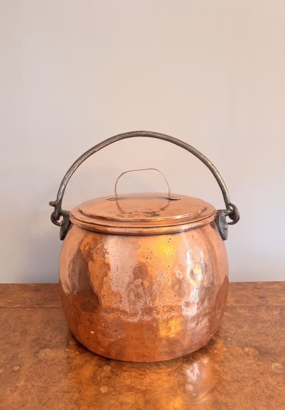 A large round hand-hammered copper pot with a fitted copper lid and a dark iron swing handle. View V