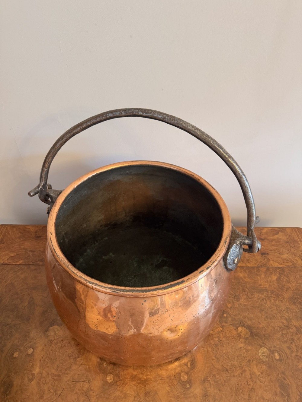 A large round hand-hammered copper pot with a fitted copper lid and a dark iron swing handle. View VI