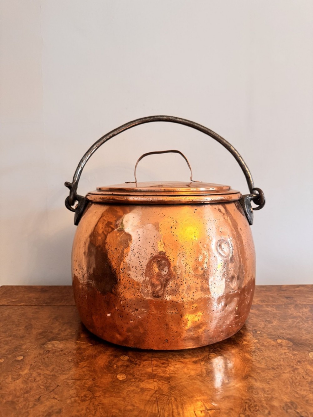 A large round hand-hammered copper pot with a fitted copper lid and a dark iron swing handle. View VII