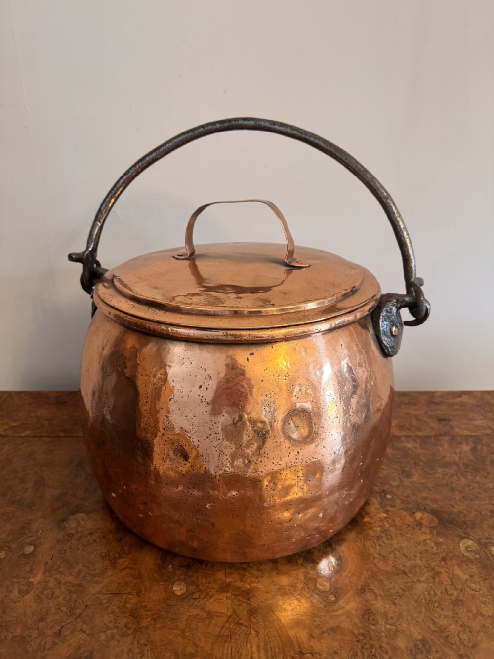 A large round hand-hammered copper pot with a fitted copper lid and a dark iron swing handle. View VIII