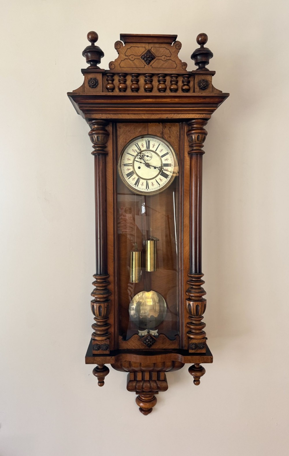 Victorian walnut Vienna regulator wall clock featuring turned side columns, decorative pediment balusters, white enamel dial, and two exposed brass weights.