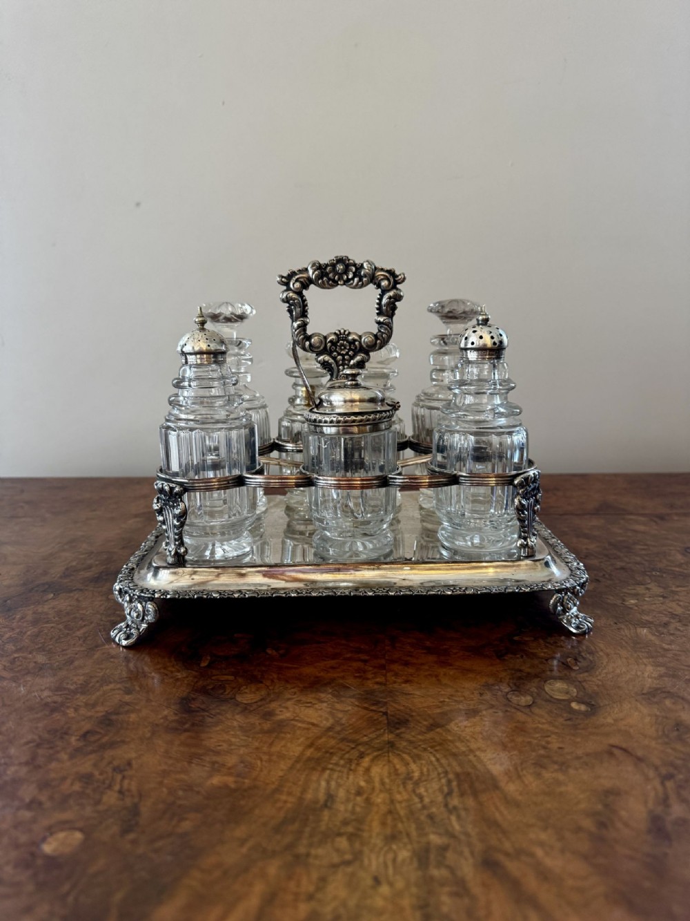 An eighteenth-century style silver-plated cruet stand holding seven faceted cut glass condiment bottles and shakers on a cast footed base.