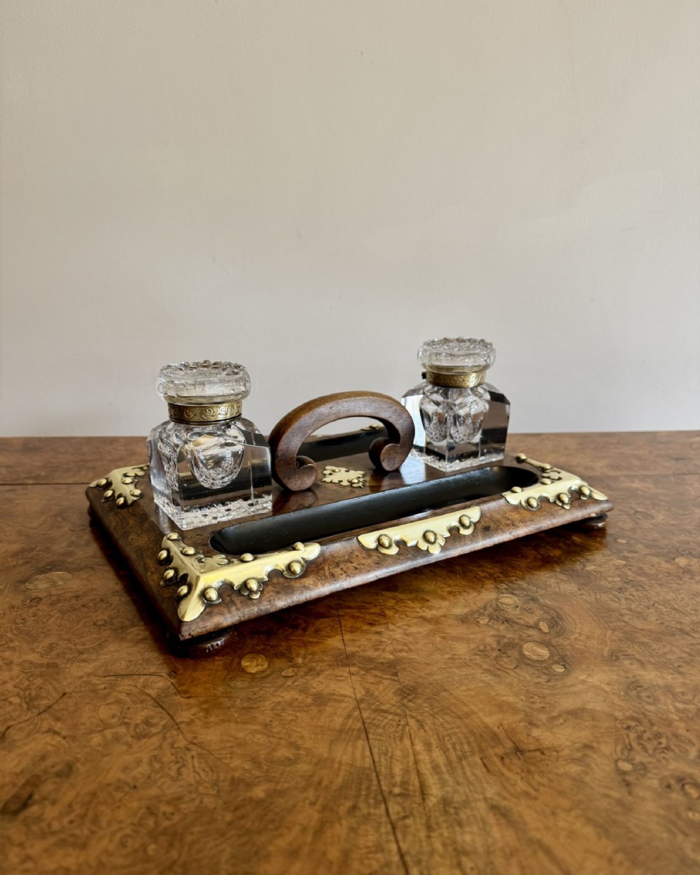 Victorian burr walnut double-sided desk set featuring two cut glass inkwells, ornate brass corner mounts, a central wood handle, and pen trays.