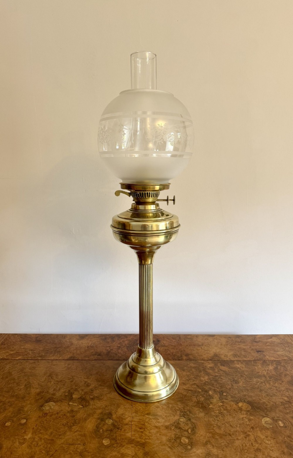 An Edwardian brass oil lamp featuring a reeded column stem, a frosted etched glass globe shade, and a clear glass chimney on a stepped round base.