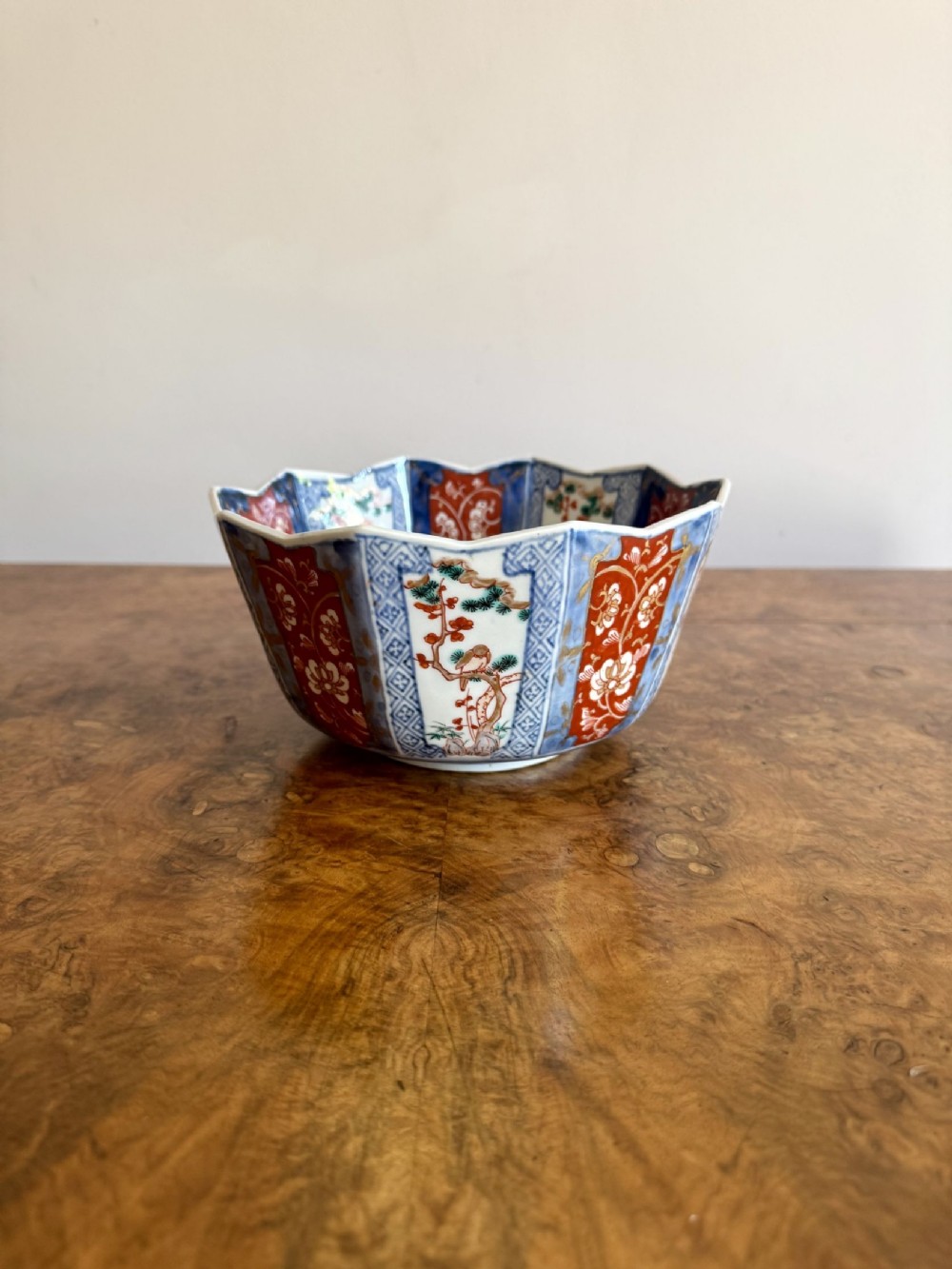A Japanese Imari porcelain bowl featuring a scalloped rim and hand-painted panels of iron red, cobalt blue, and green detailing pine tree and floral motifs.