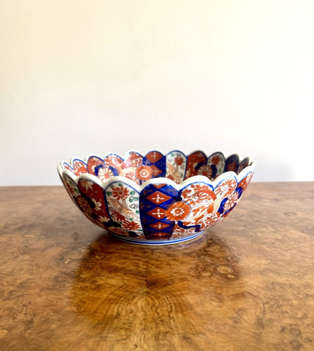 A round Japanese Imari porcelain bowl featuring a lobed scalloped rim and hand-painted panelled decoration in rust red, cobalt blue, and white.