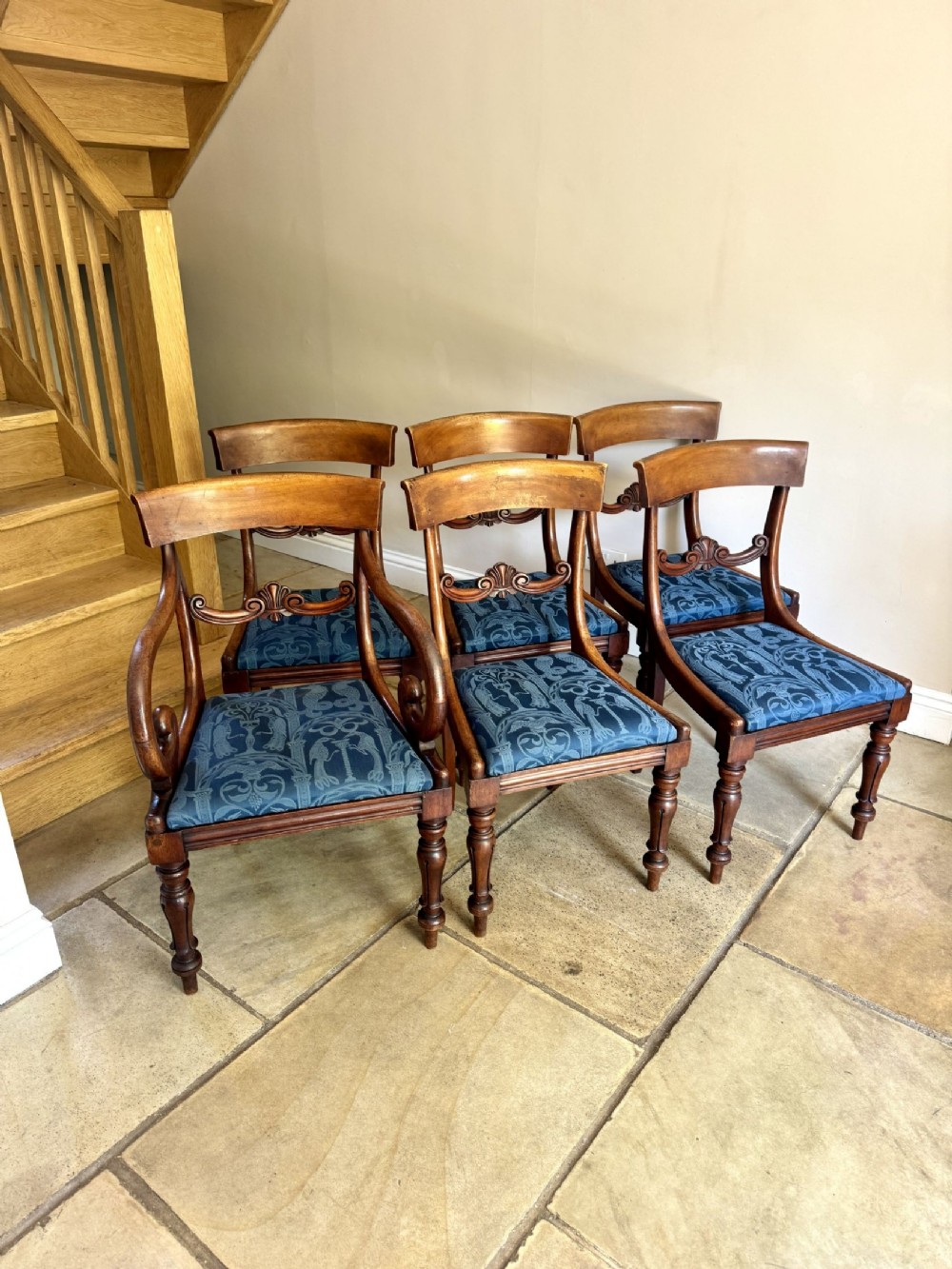 A set of six antique Regency mahogany dining chairs featuring carved back rails, turned front legs, and blue patterned upholstery.