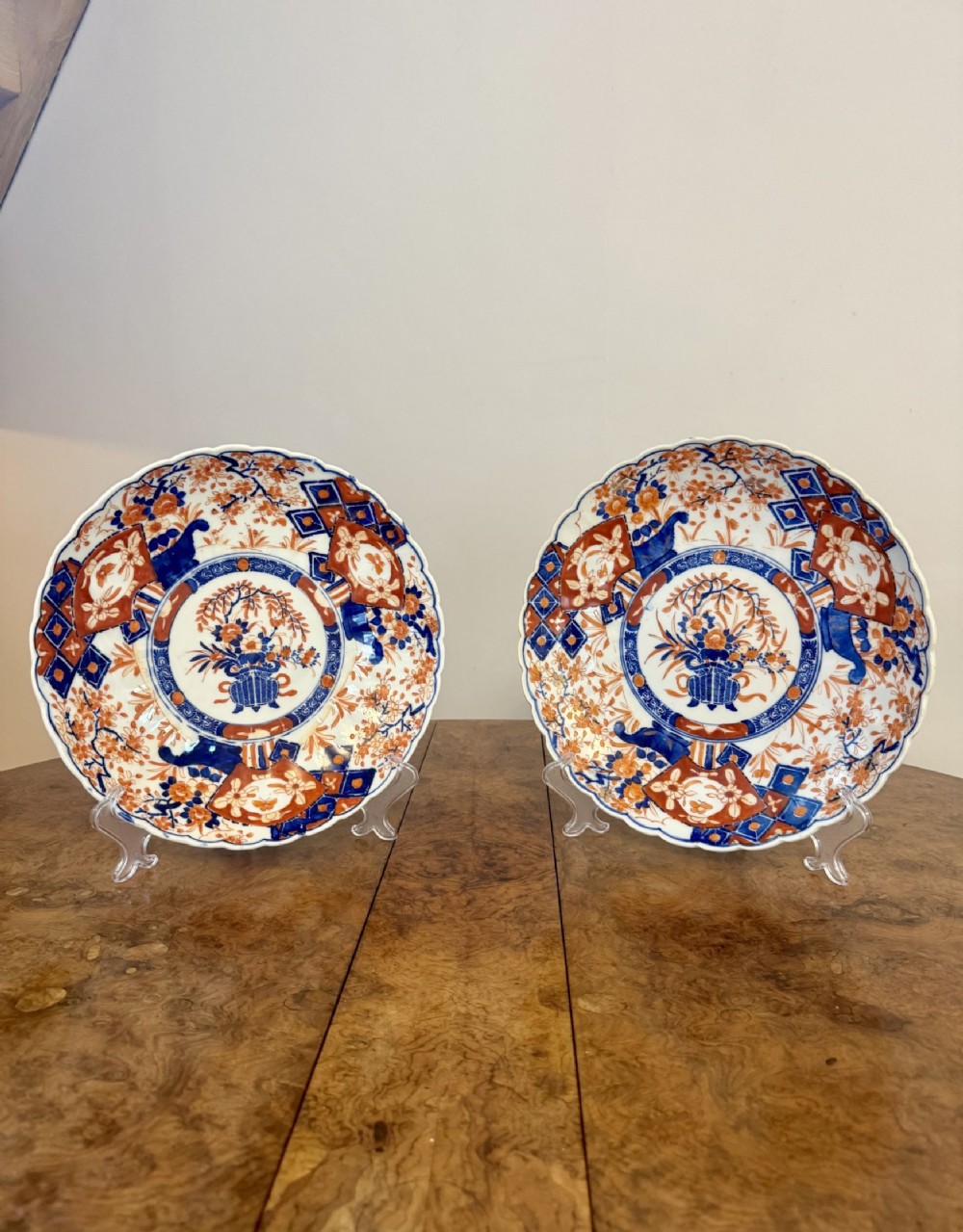 A pair of circular Japanese Imari porcelain plates with scalloped edges, decorated with hand-painted floral urn motifs in cobalt blue and iron red enamels.