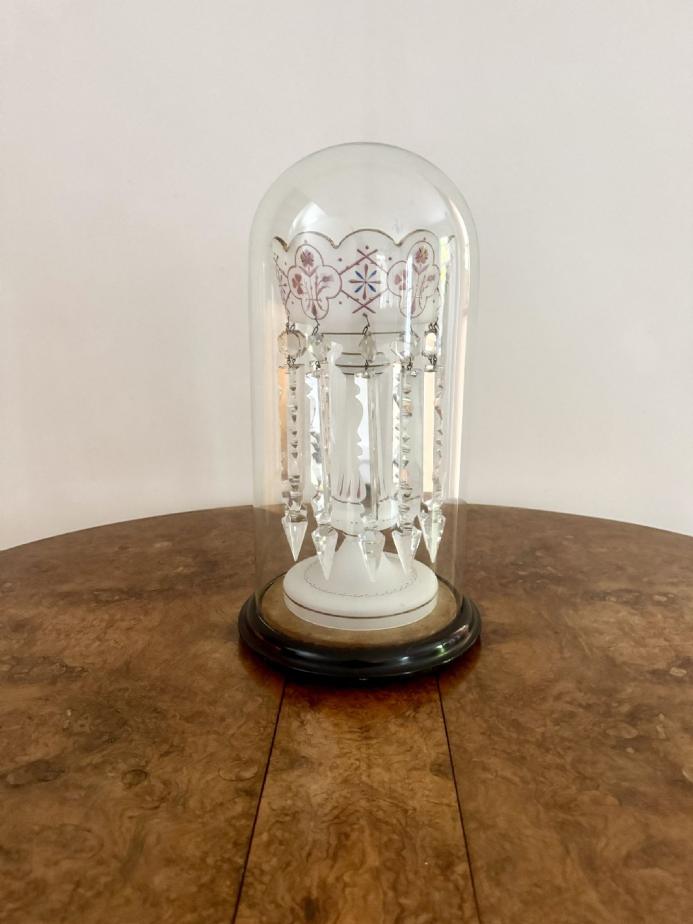 A Victorian white and enamelled glass lustre featuring hanging prism crystals housed under a protective clear glass dome on a dark wooden base.
